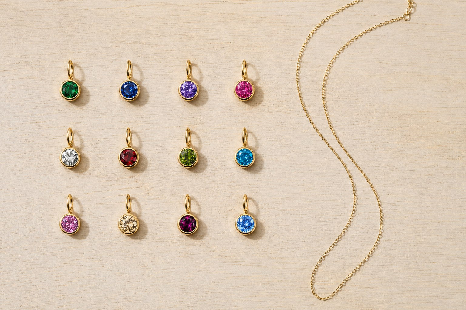 All twelve birthstone charms laid out in a grid beside a fine gold chain