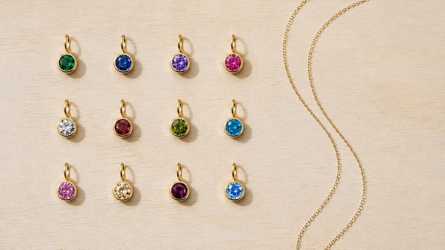 All twelve birthstone charms laid out in a grid beside a fine gold chain
