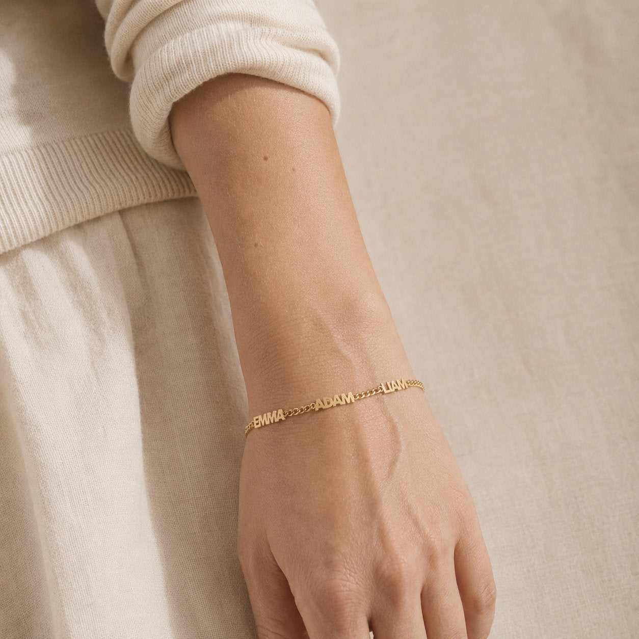 Gold curb chain bracelet with three names in block capitals worn along the top of the wrist