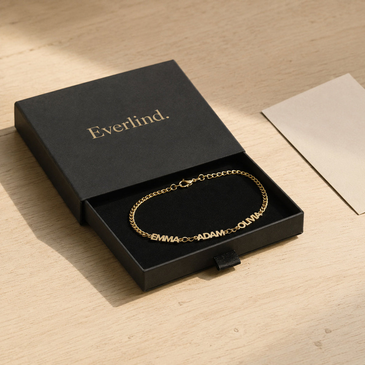 Gold name bracelet inside an open black everlind drawer box with a blank cream card
