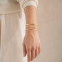 Gold name bracelet stacked on a wrist with a fine chain and a plain gold cuff
